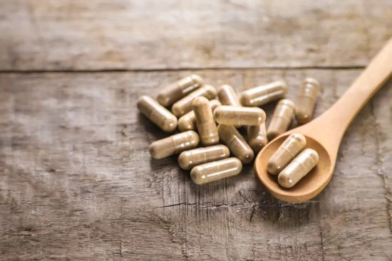 Cuillère en bois avec des gélules d'un complément alimentaire