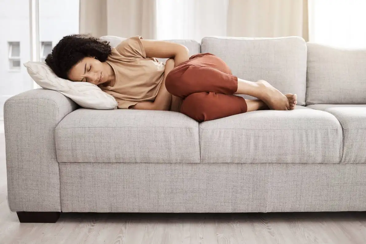 Femme allongée sur son canapée se tenant le ventre