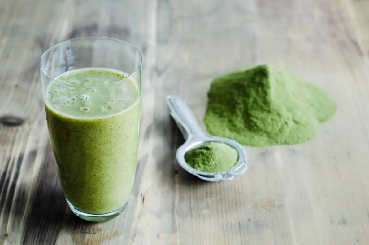 Poudre de Moringa sur cuillère et table en bois et verre de smoothie au moringa